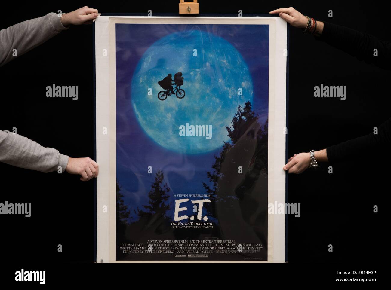 Prop Store employees hold a US One-Sheet Poster for the 1982 film 'E.T, The Extra Terrestrial' (estimate Â£800 - Â£1,200), during a preview for the Prop Store's forthcoming cinema poster auction. Stock Photo