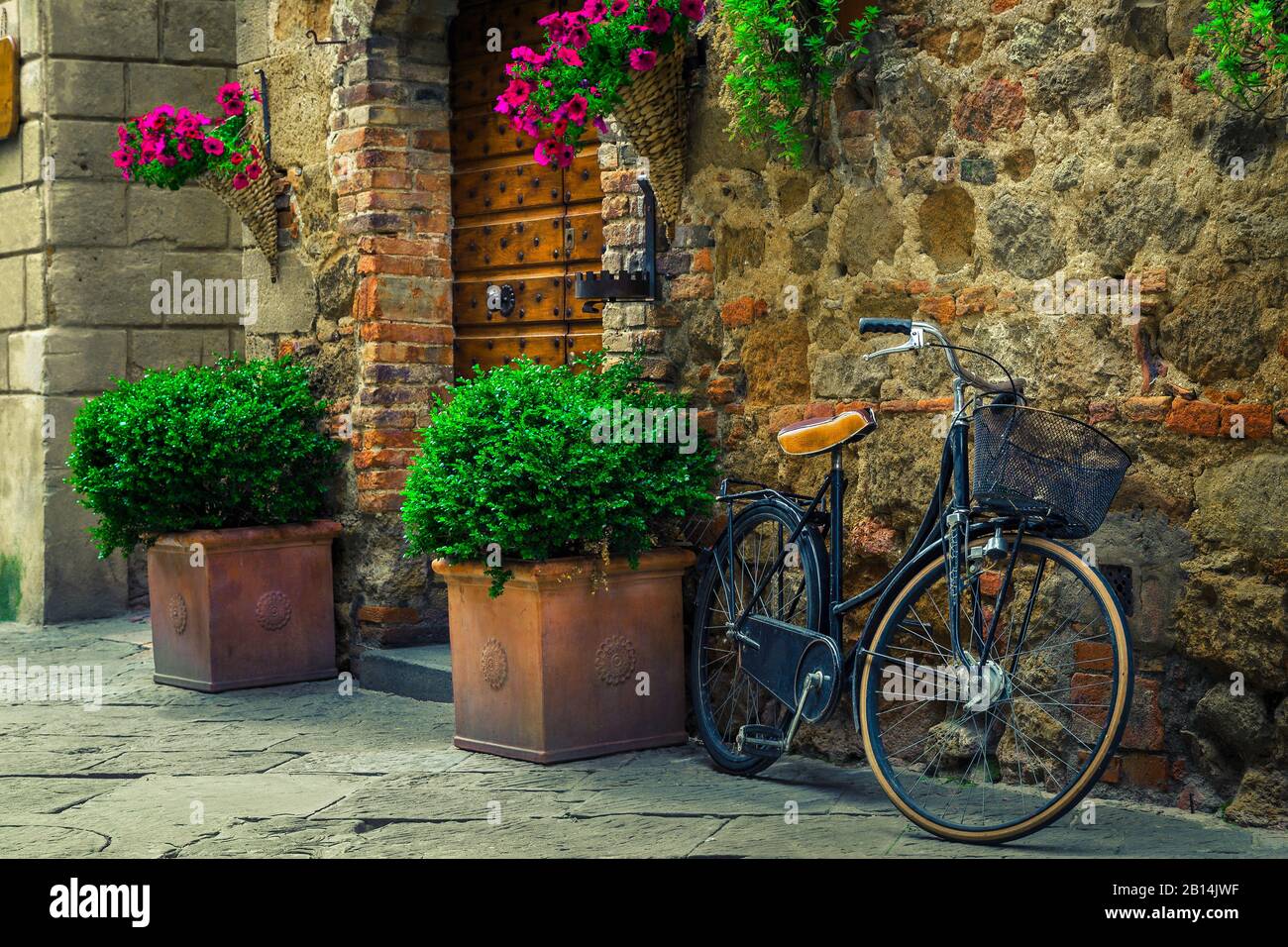 Old fashioned retro bicycle parked in the street. Entrance and wooden door decorated with flowers and flowerpots, Pienza, Tuscany, Italy, Europe Stock Photo