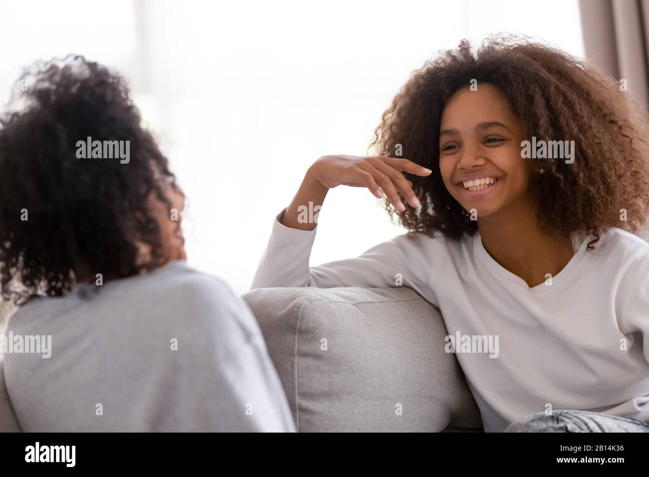 Happy african mother and daughter talking laughing sitting on sofa Stock Photo