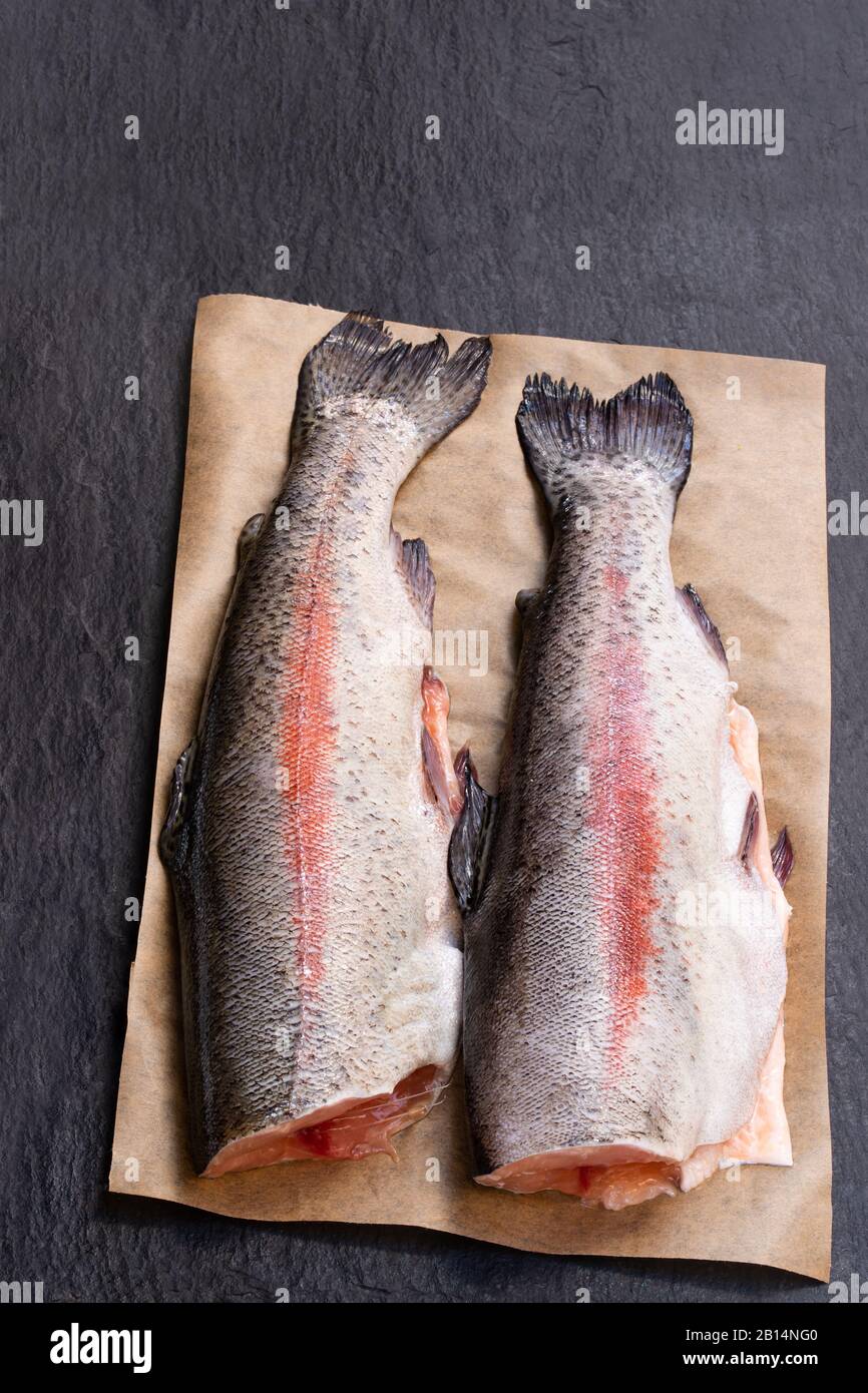 Fresh  raw rainbow trout fish with head removed on black stone background Stock Photo