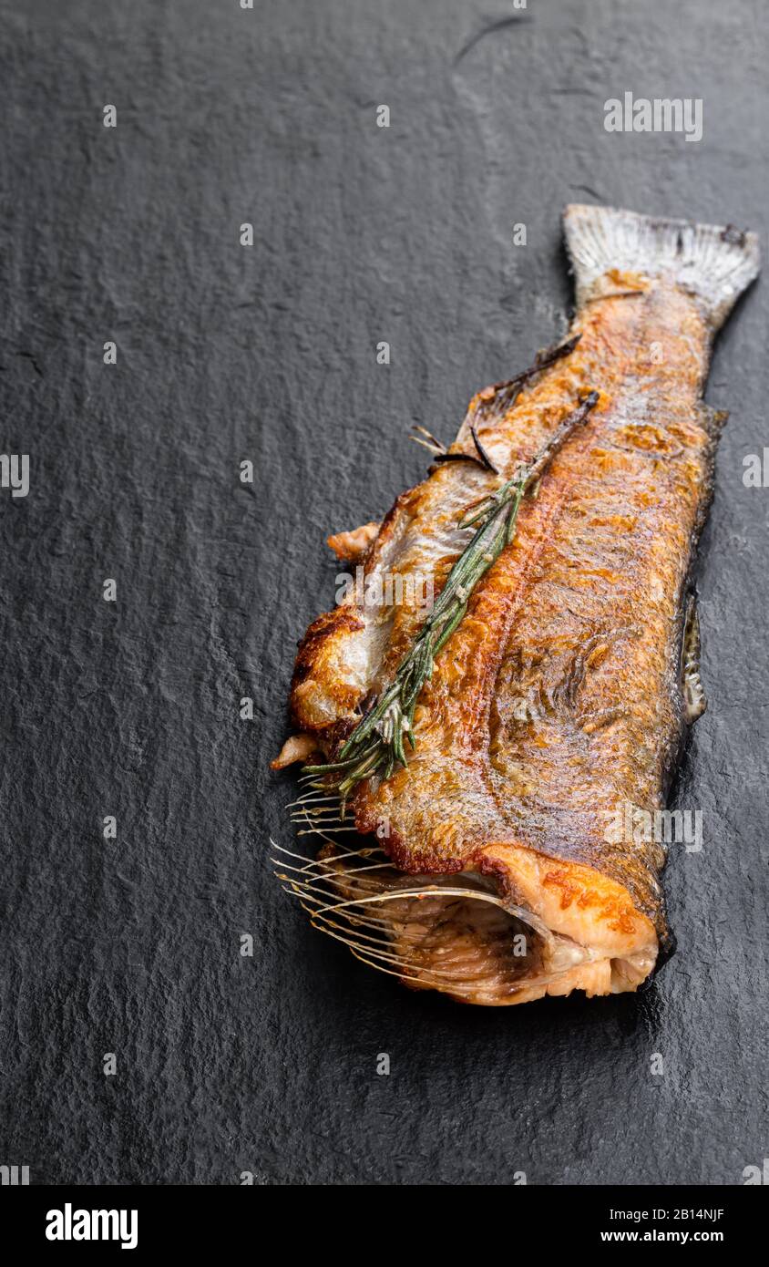 Fried trout fish with herbs on black stone background Stock Photo - Alamy
