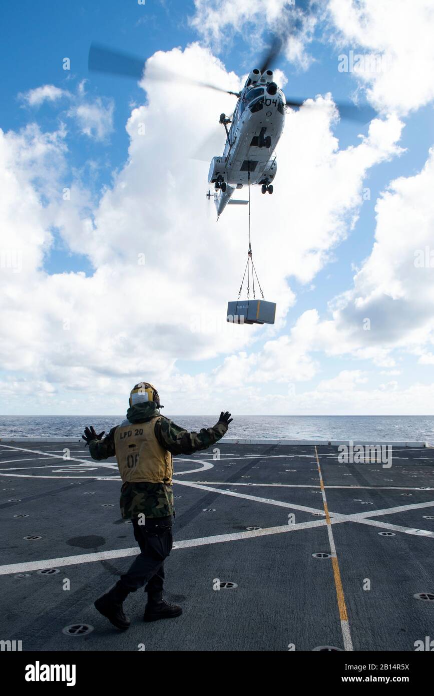 U.S. Navy Aviation Boatswain’s Mate (Handling) 3rd Class Deon Sanders, from New York, signals to an SA-330 Puma helicopter as it transports cargo to the amphibious transport dock ship USS Green Bay (LPD 20) during a vertical replenishment with the Military Sealift Command dry cargo and ammunition ship USNS Richard E. Byrd (T-AKE 4) in the Pacific Ocean, June 25, 2019. Green Bay, part of the of the Wasp Amphibious Ready Group, with embarked 31st Marine Expeditionary Unit, is operating in the Indo-Pacific region to enhance interoperability with partners and serve as a ready-response force for an Stock Photo
