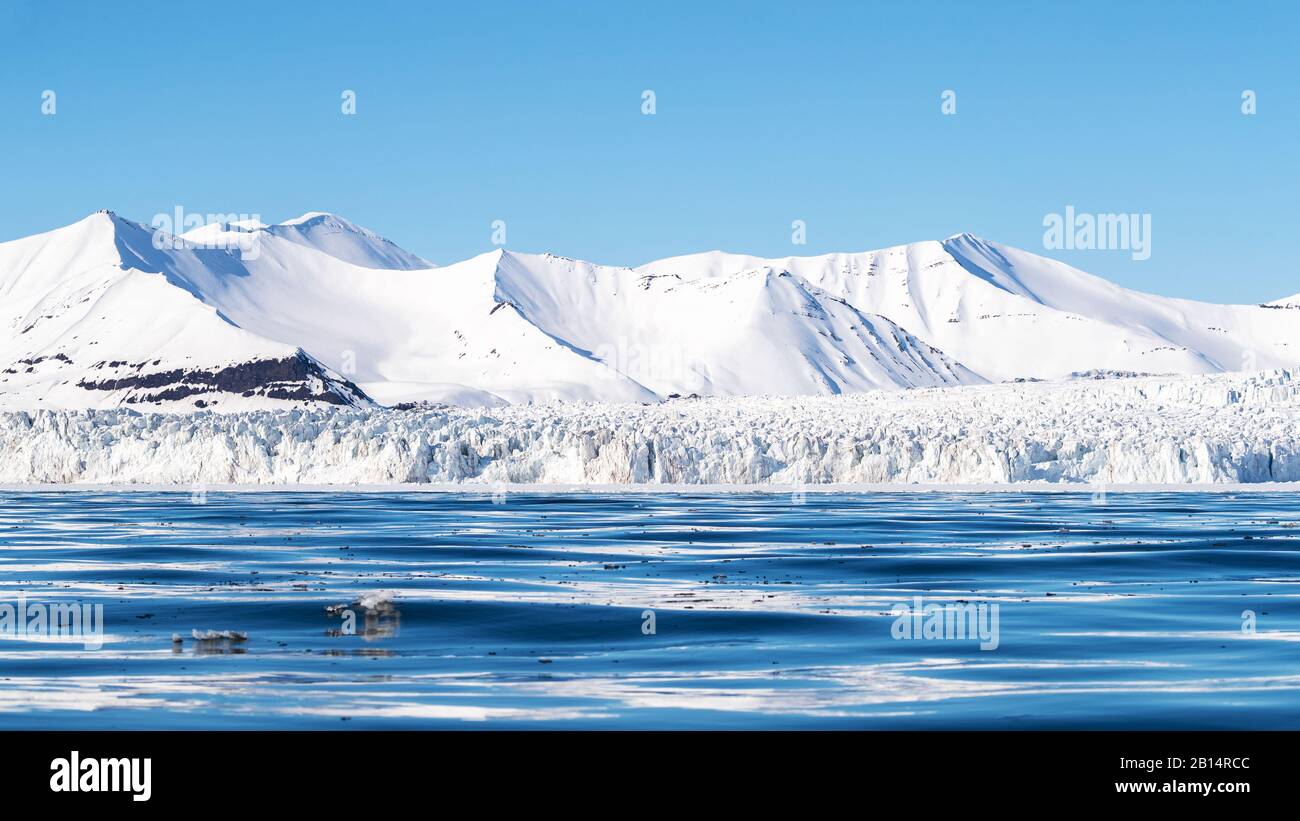 Panoramic view of a glacier and pristine snow covered mountains in Nordfjorden, Svalbard. Stock Photo