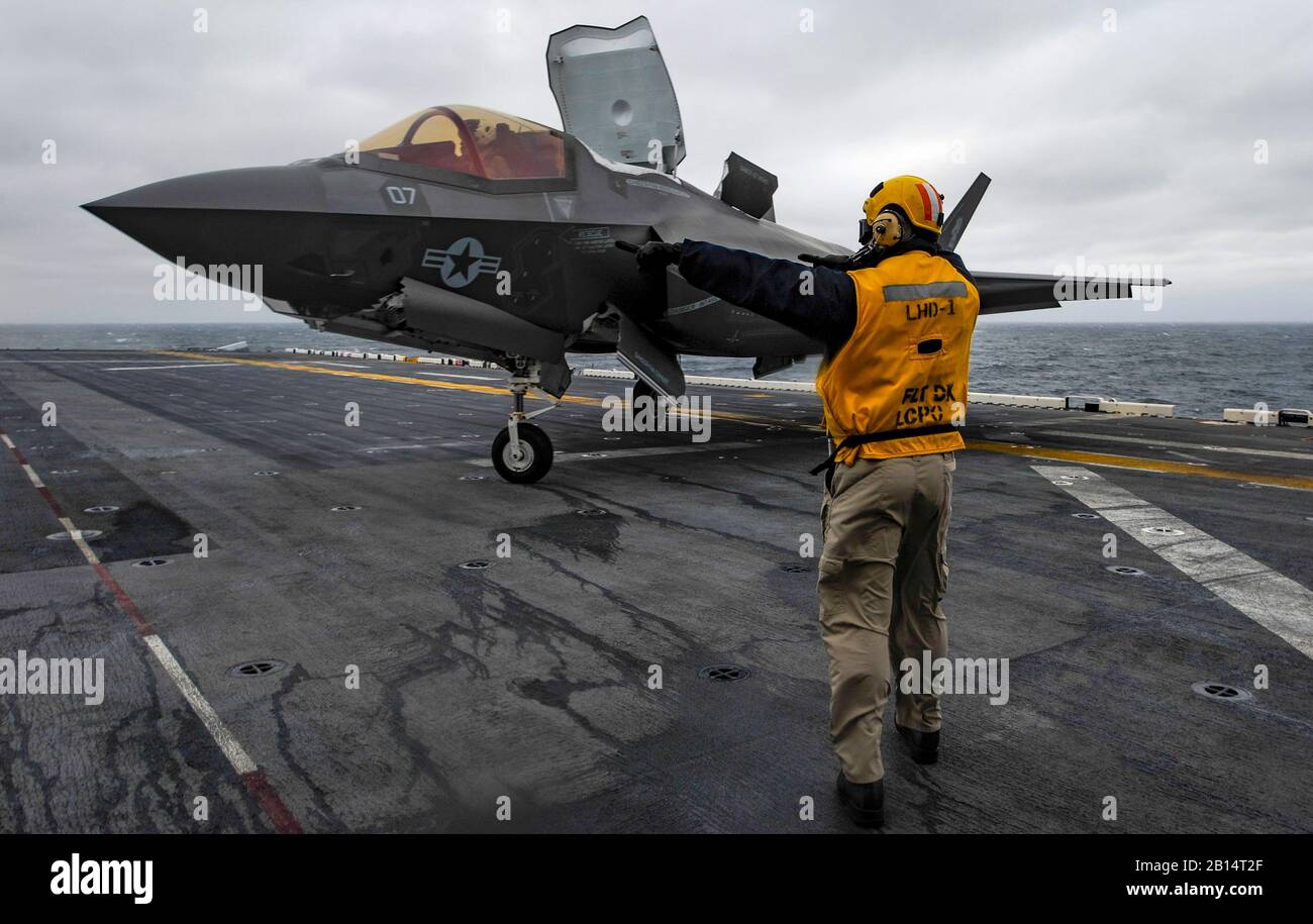 U.S. Navy Chief Aviation Boatswain's Mate (Handling) John Jacob directs an F-35B Lightning II with Marine Fighter Attack Squadron (VMFA) 121 on the flight deck of the amphibious assault ship USS Wasp (LHD 1) in the East China Sea March 5, 2018, marking the first time the aircraft has deployed aboard a U.S. Navy ship and with a Marine Expeditionary Unit in the Indo-Pacific. VMFA-121, assigned under the Okinawa-based 31st Marine Expeditionary Unit, will remain embarked aboard Wasp for a regional patrol meant to strengthen regional alliances, provide rapid-response capability, and advance the Up- Stock Photo