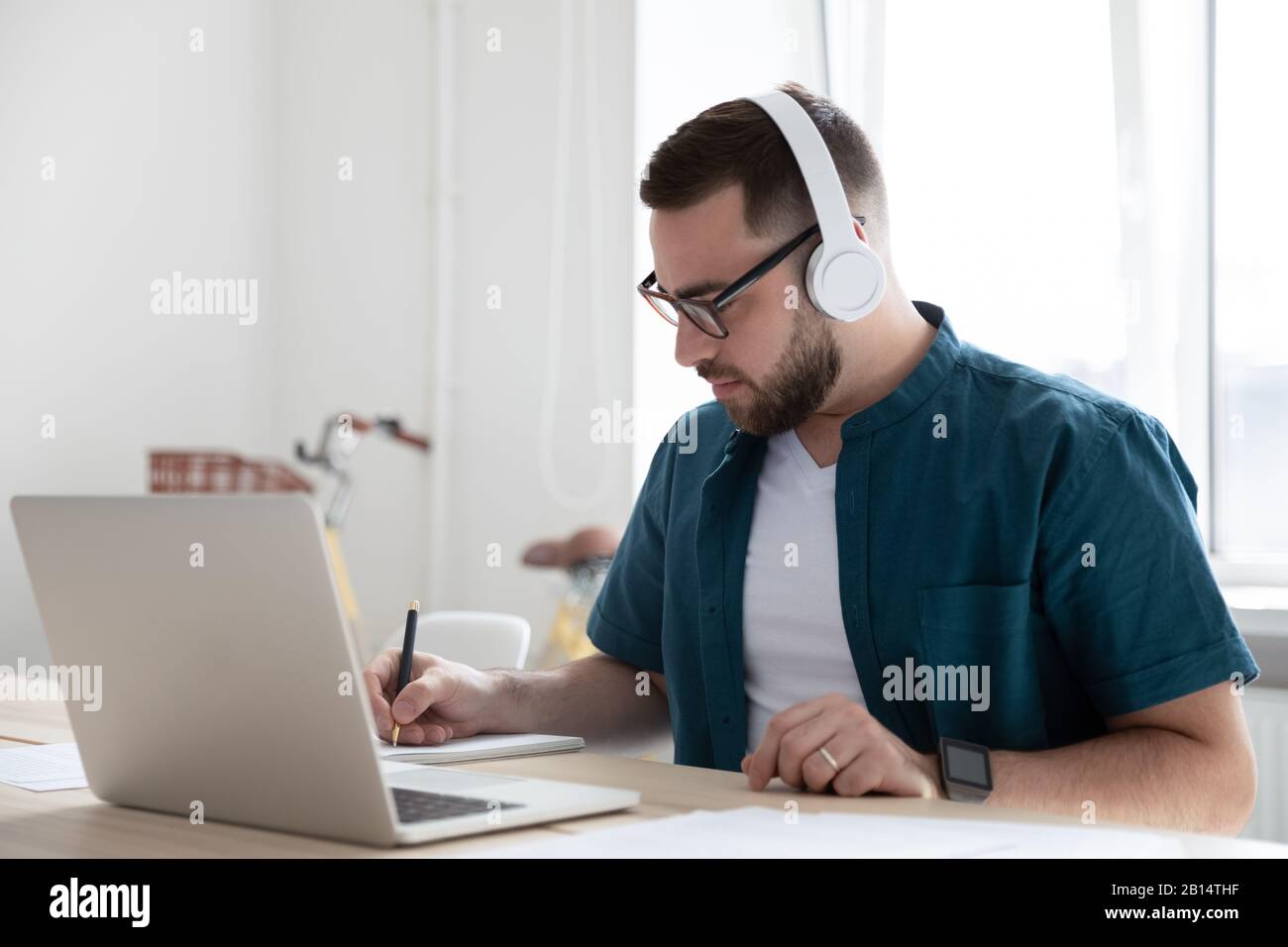 Focused young man watching educational webinar, writing down notes. Stock Photo