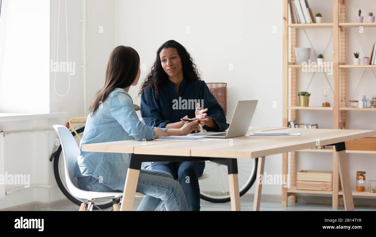 Young mixed race coworkers discussing working issues together at workplace. Stock Photo