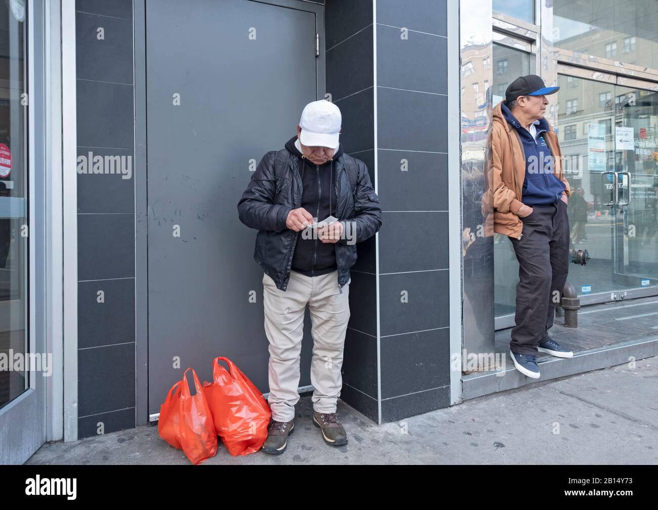 A  man out shopping stops to check a New York State lottery ticket on Main St. in Chinatown, Flushing, New York City. Stock Photo