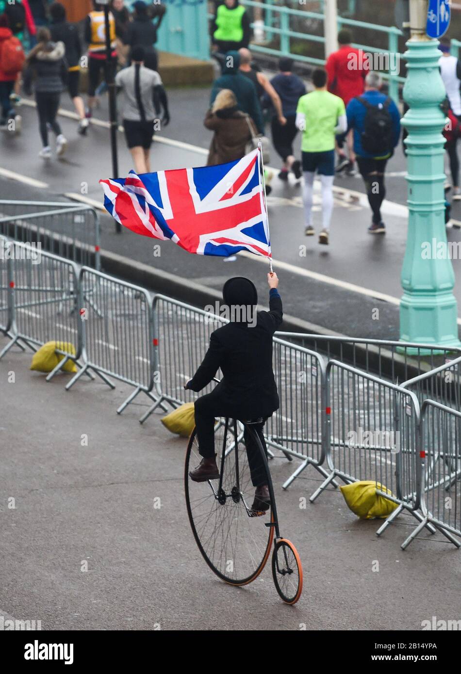 Brighton UK 23rd February 2020 - A penny farthing cyclist makes his way to the start  of The Grand Brighton Half Marathon in wet and windy weather conditions . Over ten thousand runners took part and this years official charity partners is The Sussex Beacon which provides specialist care and support for people living with HIV  : Credit Simon Dack / Alamy Live News Stock Photo