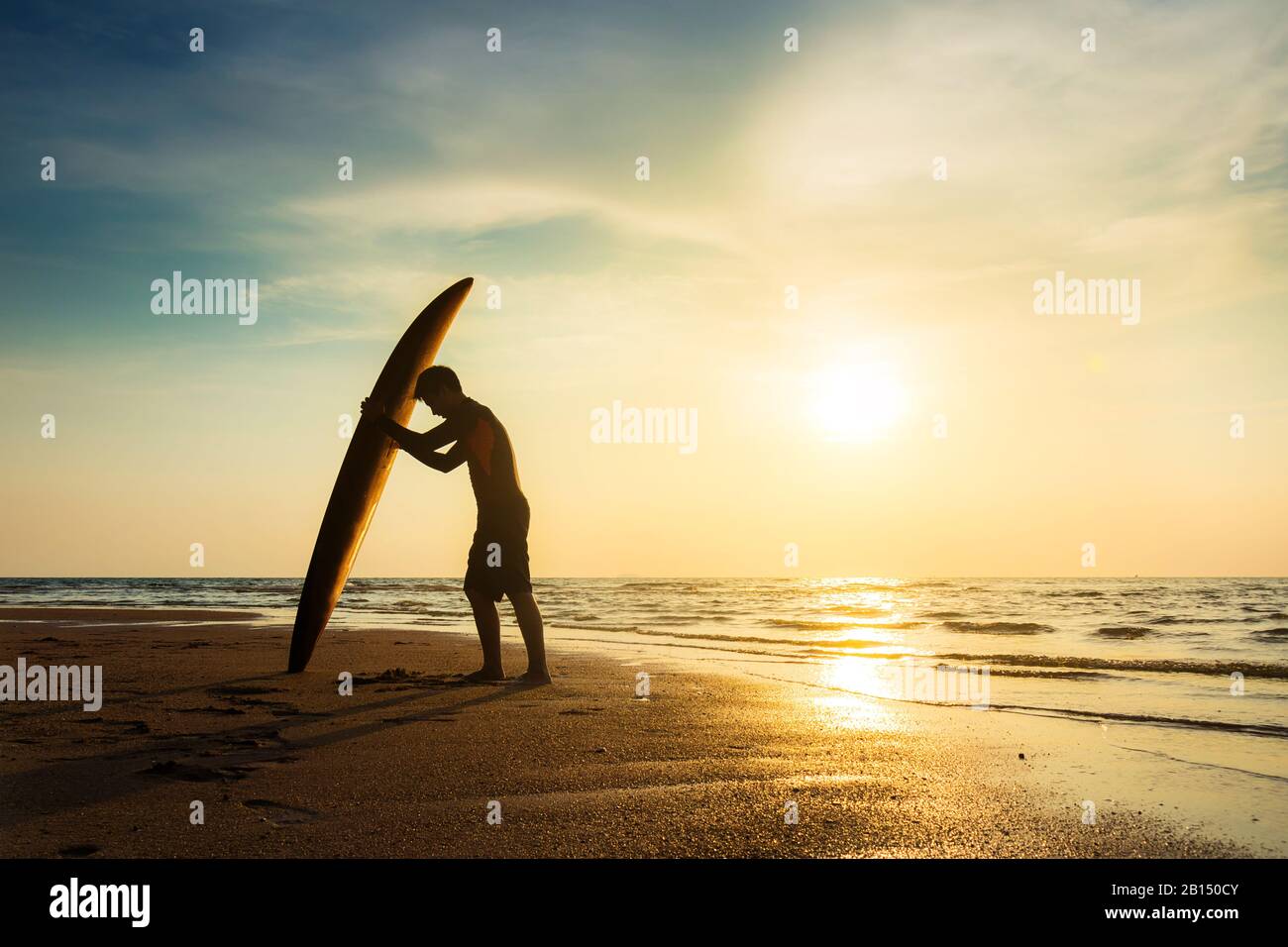 Surfing for water sport outdoor activity lifestyle concept. Silhouette of young happy surf man at white beach with surfboard. Surfer on the beach Stock Photo