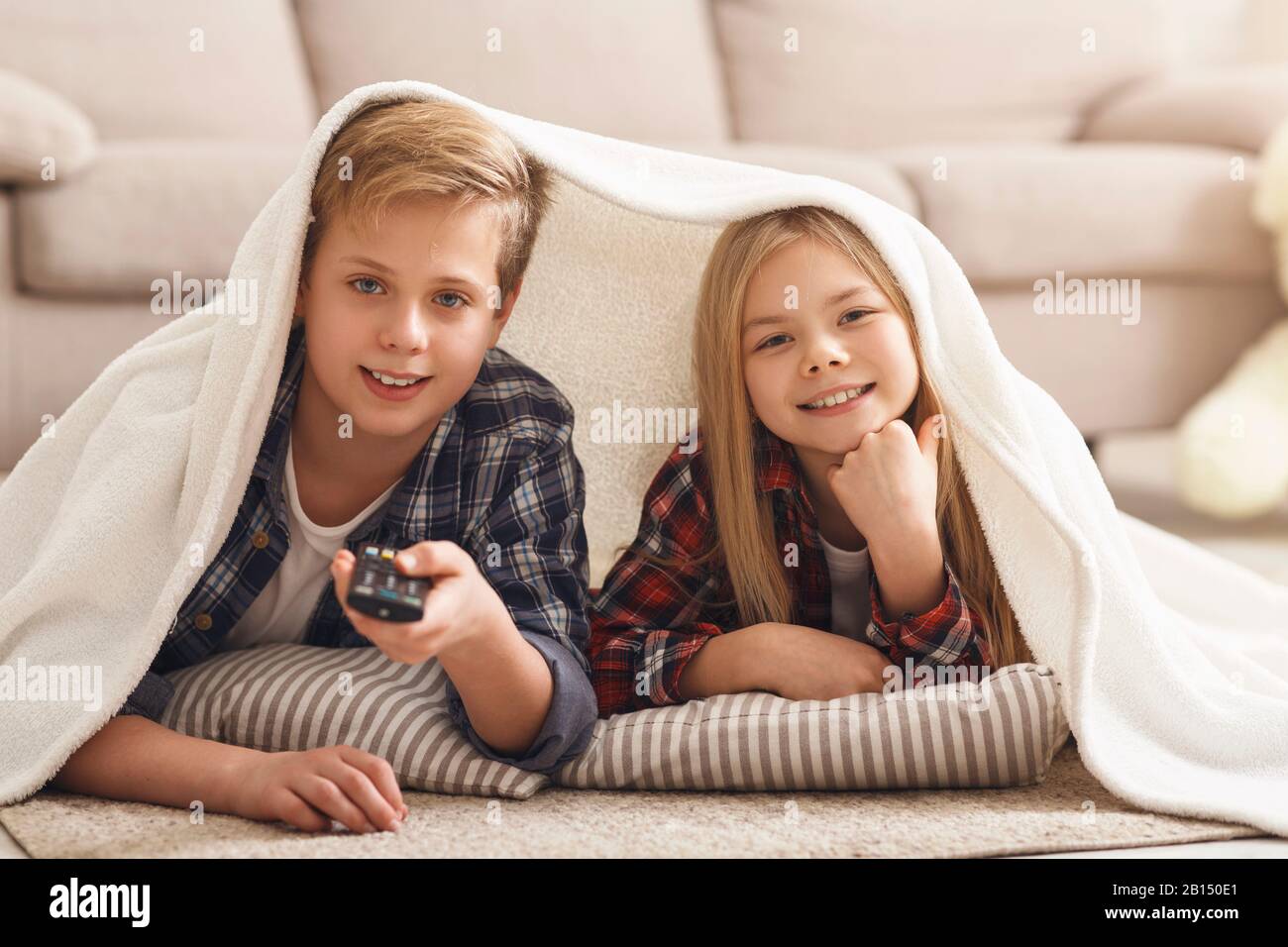 Happy Girl And Boy Watching TV Lying On Floor Indoor Stock Photo