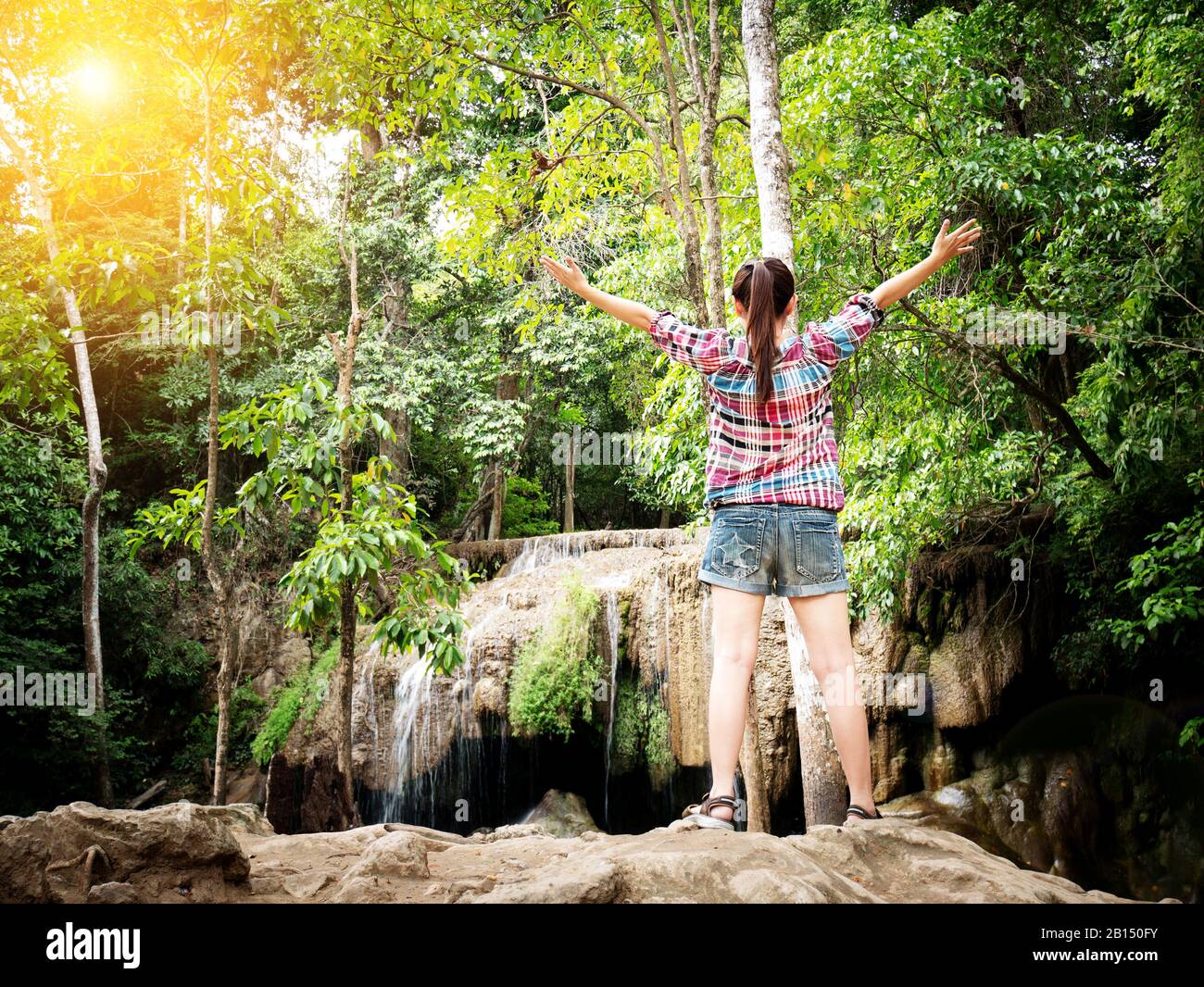 Journey vacation tourist concept - Happy young female traveler open arms with happiness in front of beautiful waterfall with nature. Having a great va Stock Photo