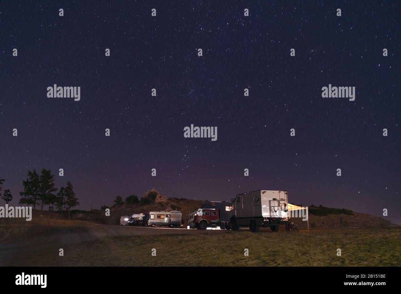 Many motorhome vehicles parked on the beach in night time. Dark starry sky with shining stars. Camper lifestyle Stock Photo