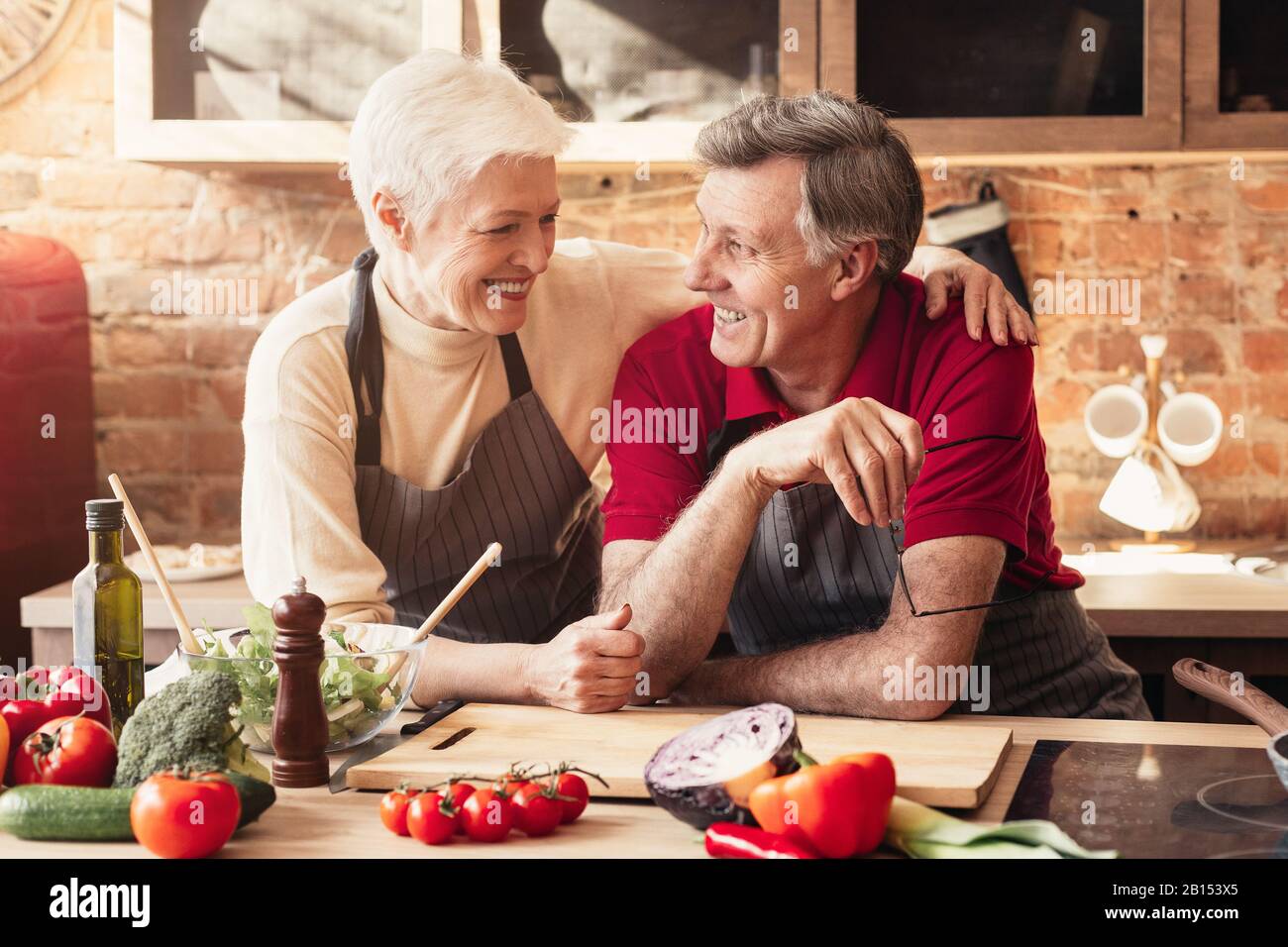 Happy elderly couple embracing in kitchen while cooking dinner together ...