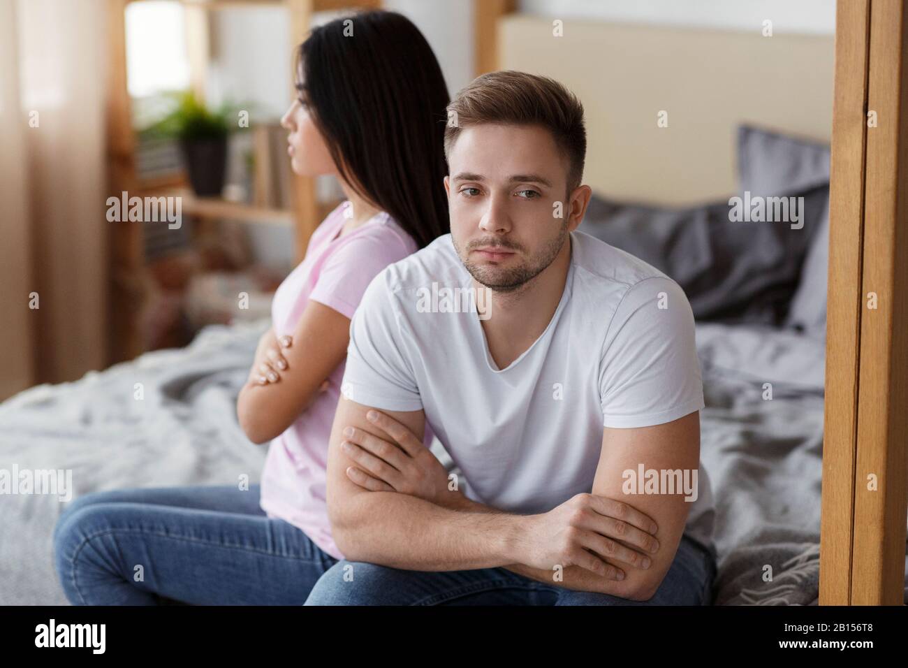 Offended Couple Sitting On Different Sides Of Bed At Home Stock Photo