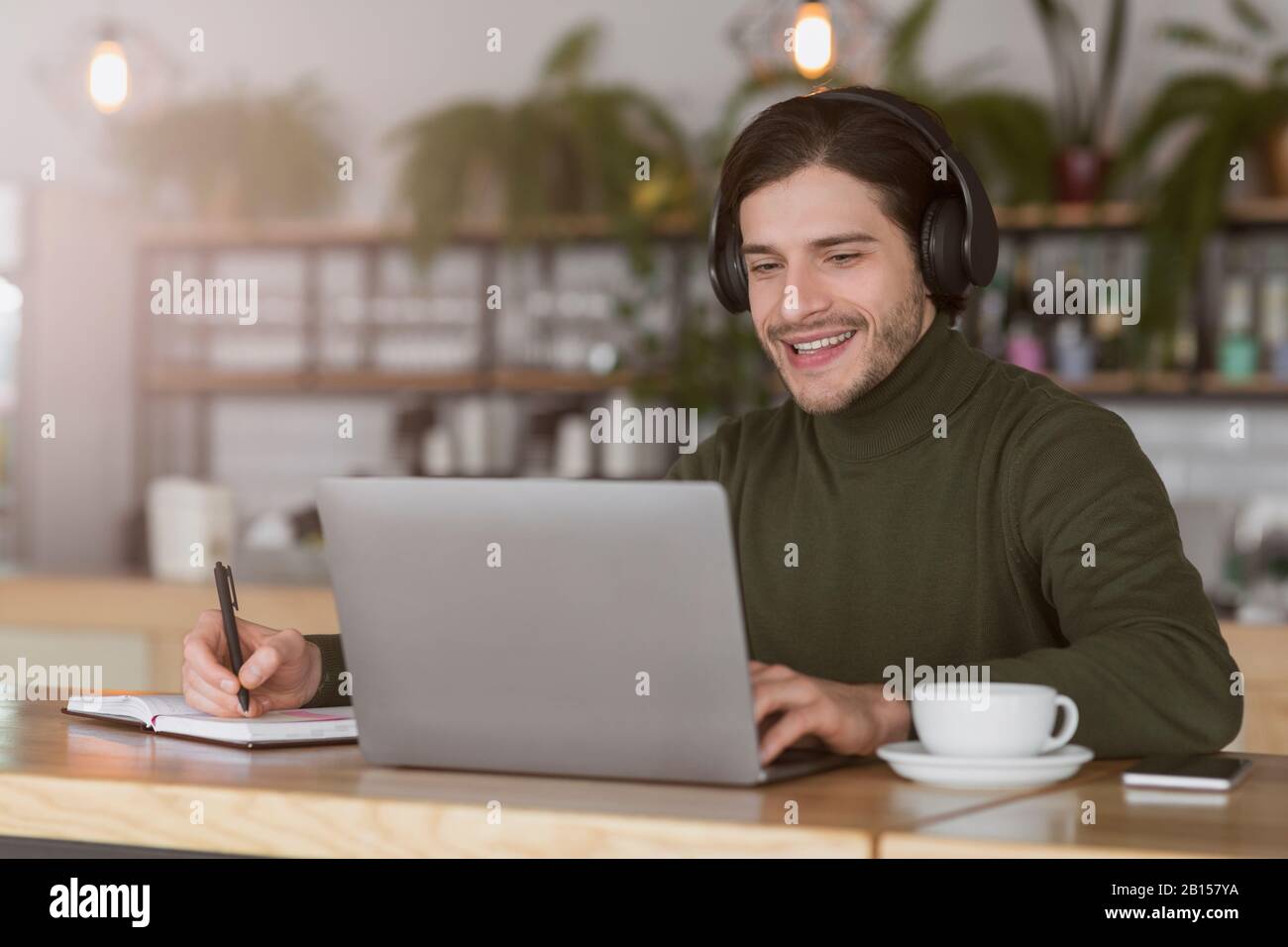 Young guy in wireless headphones studying online, using laptop Stock Photo