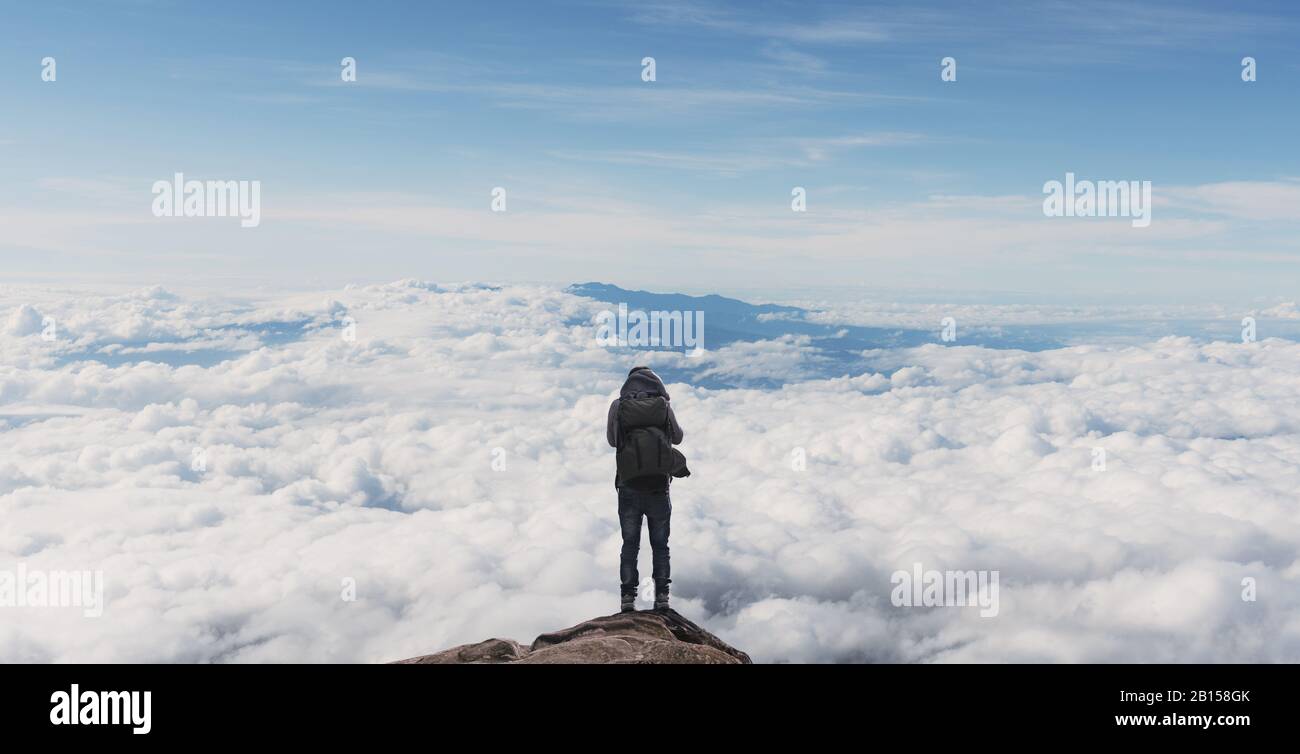 a man with backpack standing on mountain top over clouds. Success, achievement and outdoor adventure concepts Stock Photo