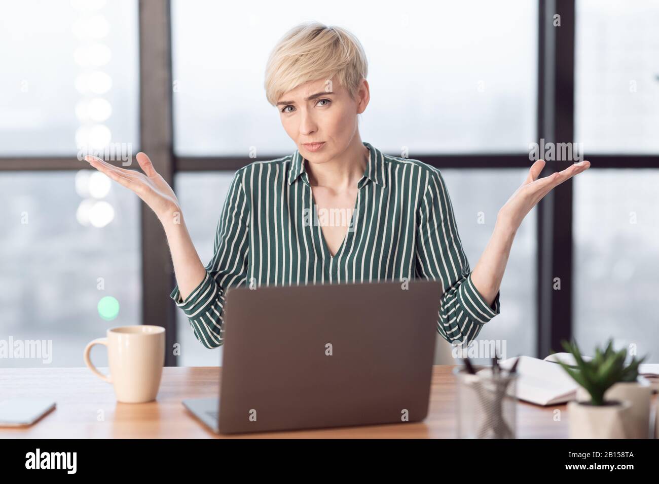 Puzzled Lady Shrugging Shoulders Gesturing With Hands Sitting In Office Stock Photo