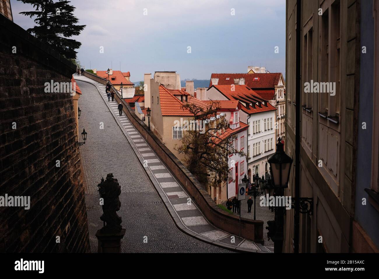 A view from Radnické schody & Ke Hradu, people walking up the pretty paved street to Prague castle with a backdrop of the red roofs of the old town. Stock Photo