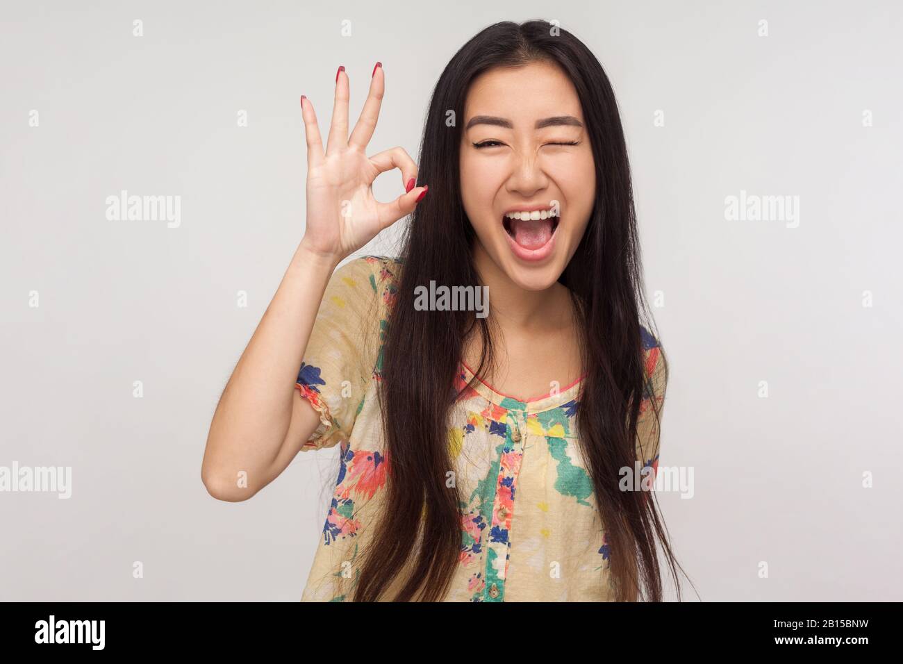 Ok I got it! Playful delighted asian girl with brunette hair in summer blouse winking joyfully and showing okay gesture, agreeing with suggestion, emo Stock Photo