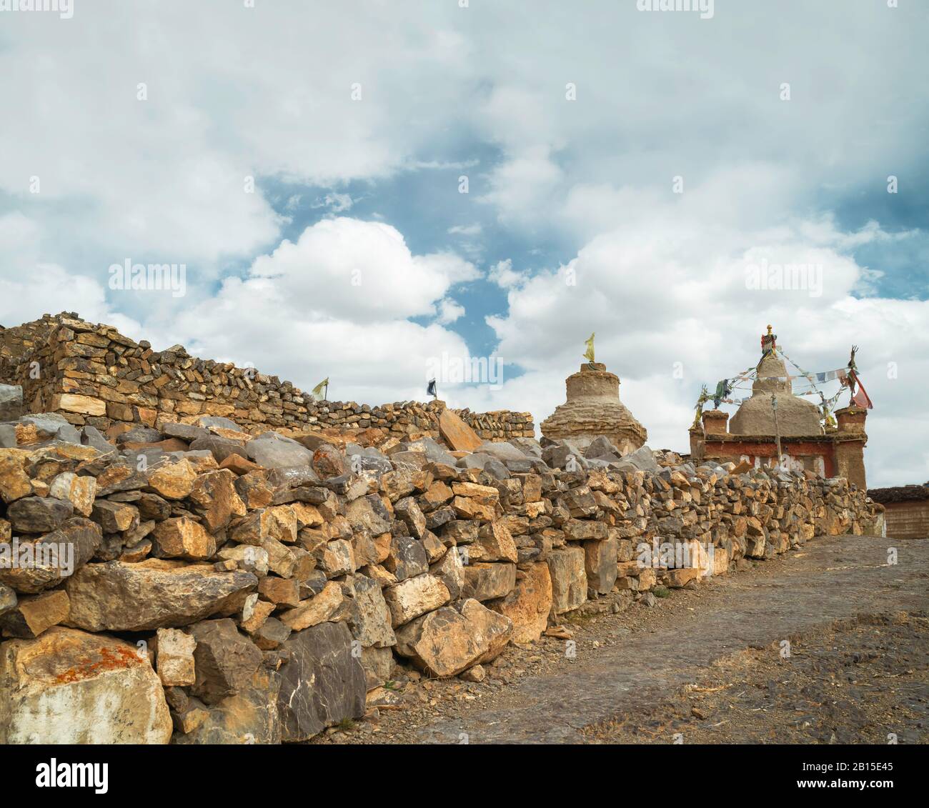 Traditional dry stone wall culminating in Buddhist gompa and chorten under clouded blue sky in Himalayan village of Tashigong, Himachal Pradesh, India. Stock Photo