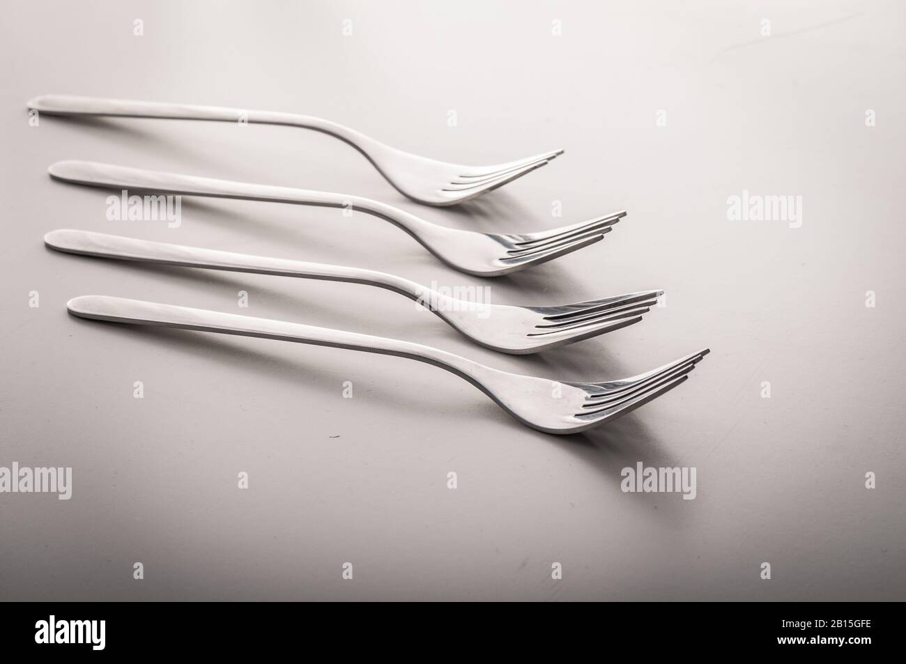 Many shiny gourmet restaurant quality design silver forks laying elegant in a row on a white dining table with copyspace - Concept of dinning cutlery, Stock Photo