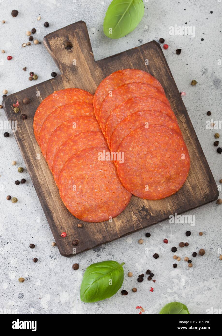 Spicy pepperoni salami with basil and pepper on wooden chopping board