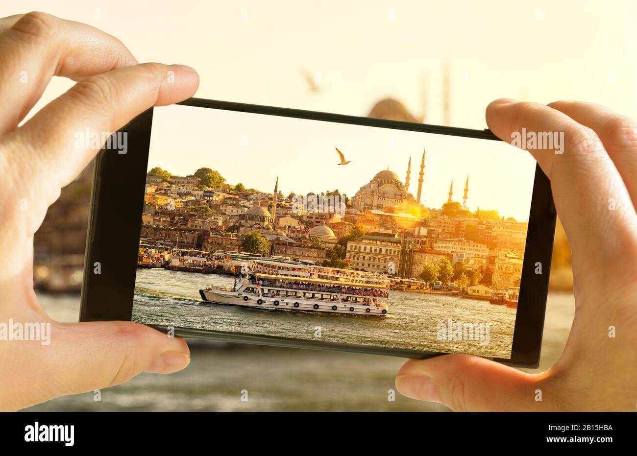 Istanbul at sunset, Turkey. Taking photo of Golden Horn by cell phone. Tourist boat sails in the Istanbul center. Sunny picture of eastern landscape o Stock Photo