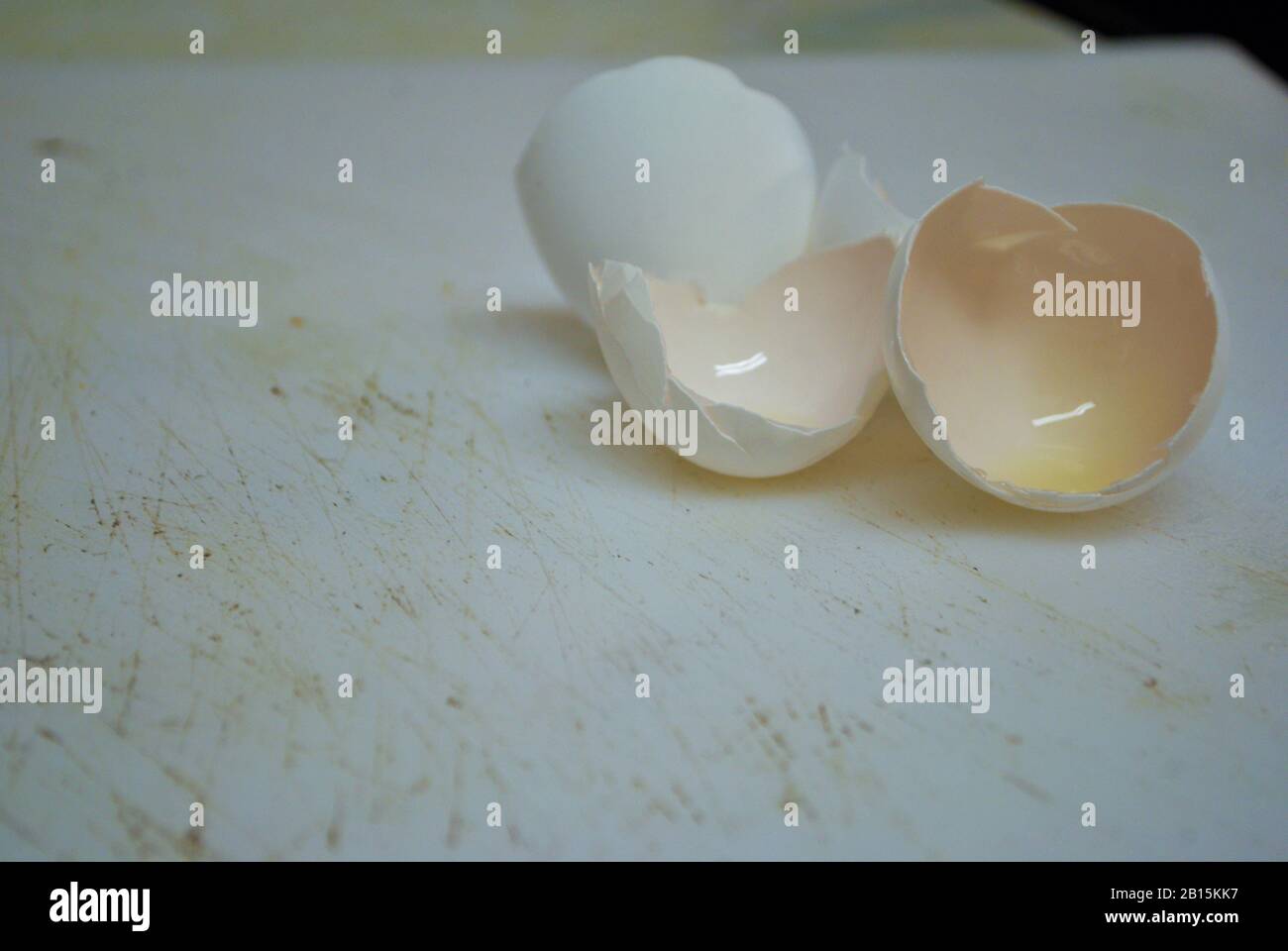 Close up of two cracked eggshells on a well used cutting board Stock Photo