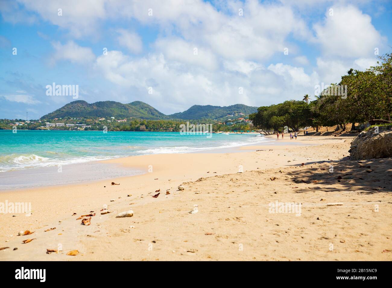 Sand, blue sea, people and hills in the distance, shadows cast by almond trees and the cloudy azure blue sky Stock Photo