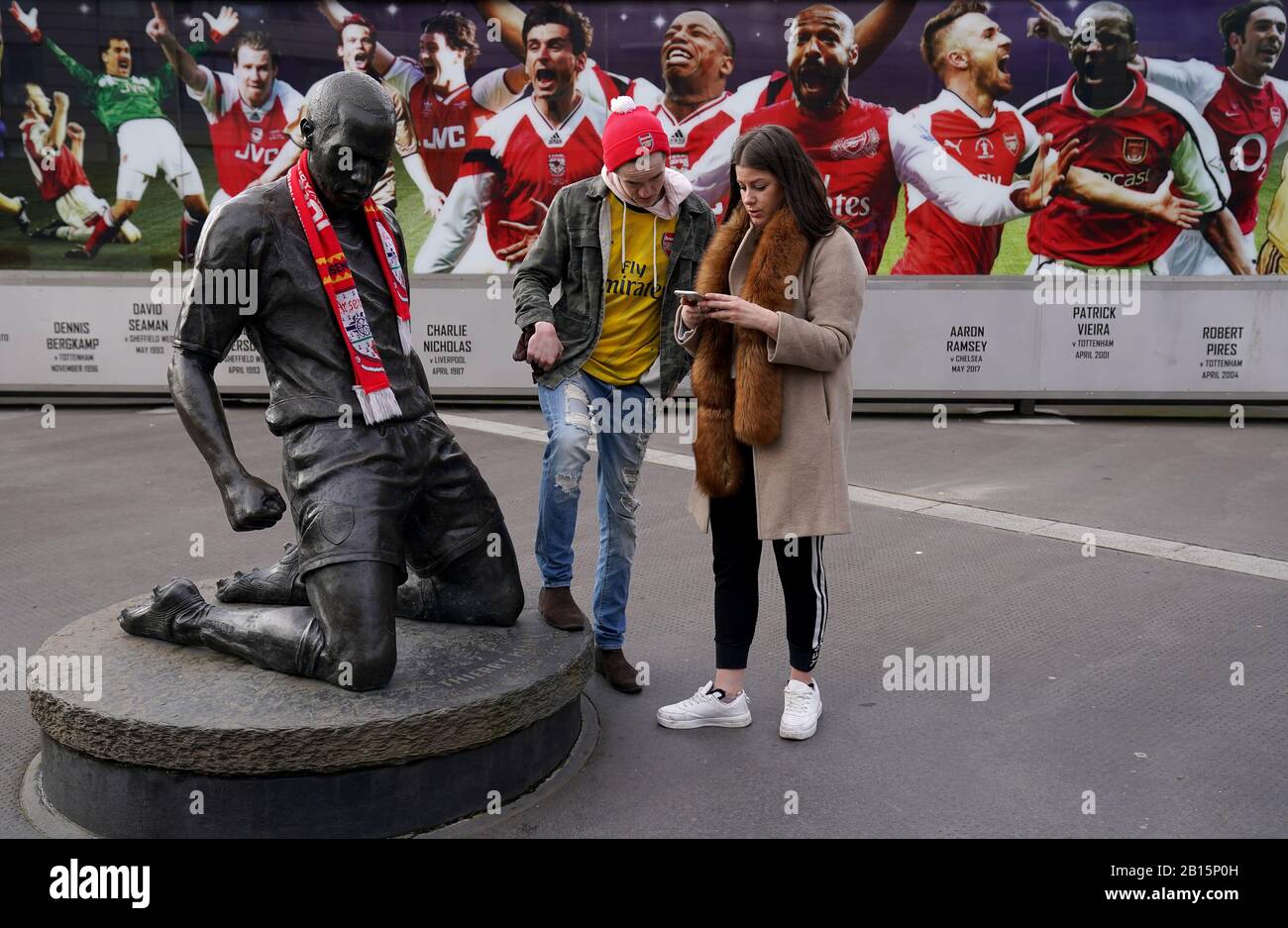 Arsenal fans stand near the Thierry Henry statue outside the ground