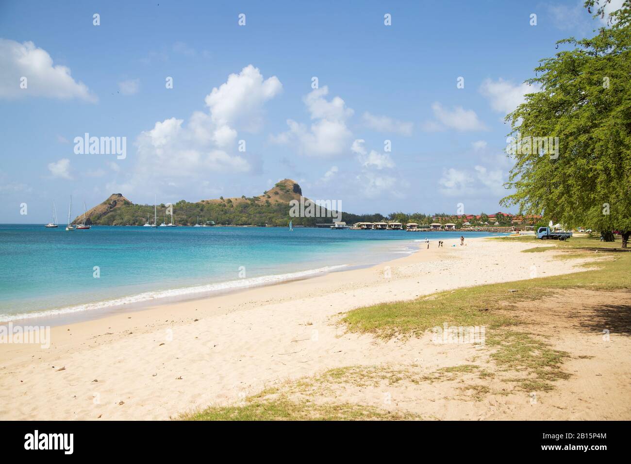 White sand, blue sea and sky, people, grassy lawn near beach, hotel, green gum trees and pigeon island national landmark, famous peninsula in distance Stock Photo