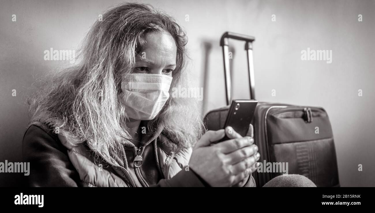 Woman in protective mask sits near luggage in airport. Novel COVID-19 coronavirus outbreak, epidemic in Wuhan, China. Person prevents flu and corona v Stock Photo