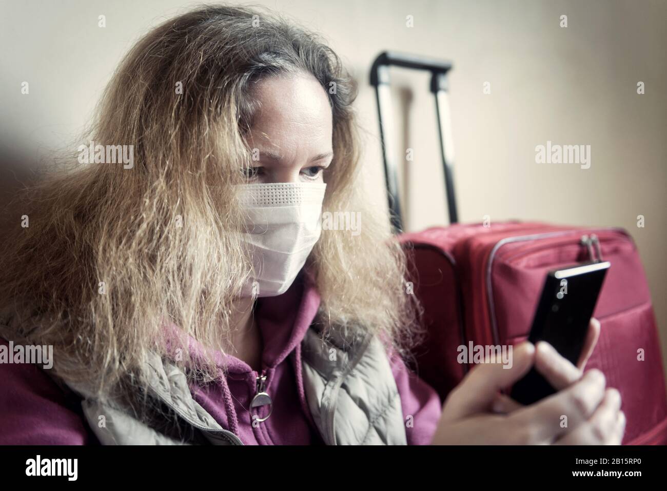 Woman in medical mask sits near luggage in airport. Novel COVID-19 coronavirus outbreak, epidemic in Wuhan, China. Person prevents flu and corona viru Stock Photo