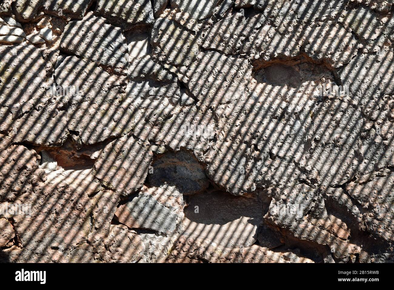 Shadows fall in parallel diagonal lines on rough volcanic stone wall. Natural, authentic. Stock Photo