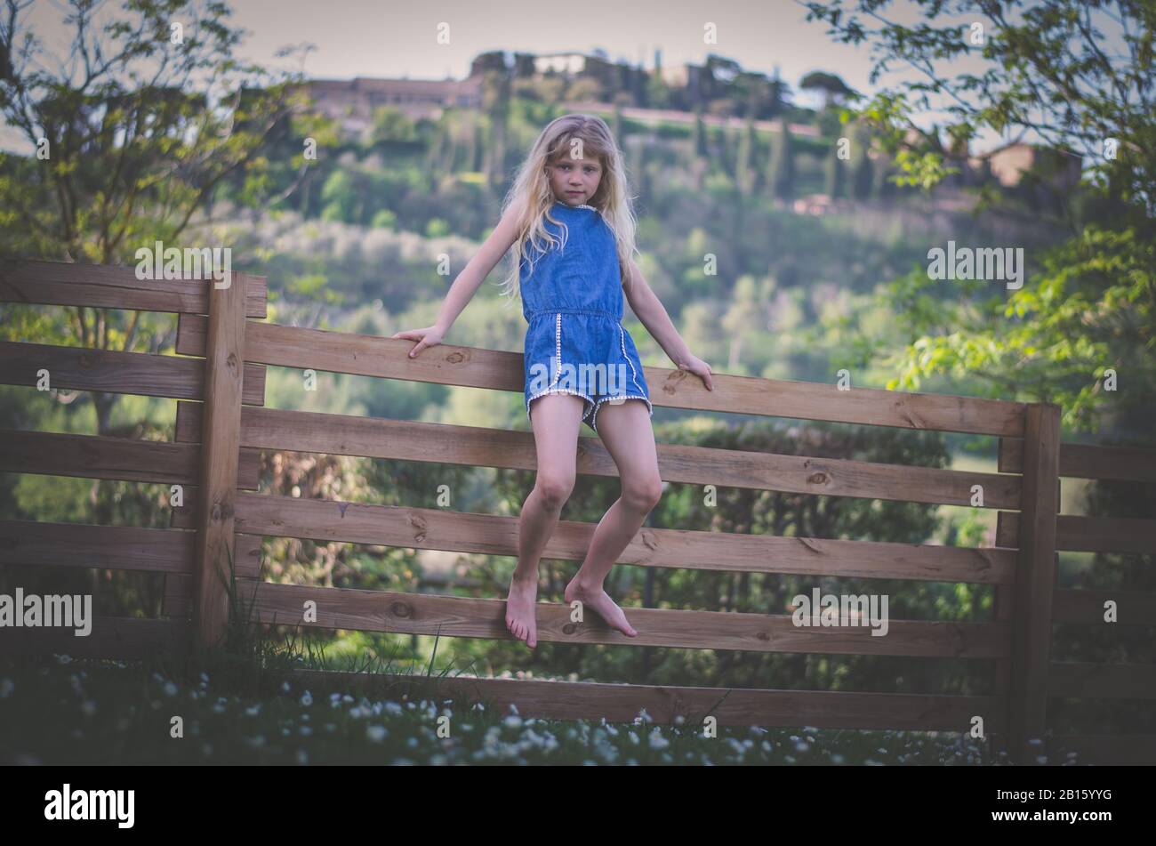 adorable little child sitting at the wooden fence in green nature in beautiful romantic italian Tuscany Stock Photo