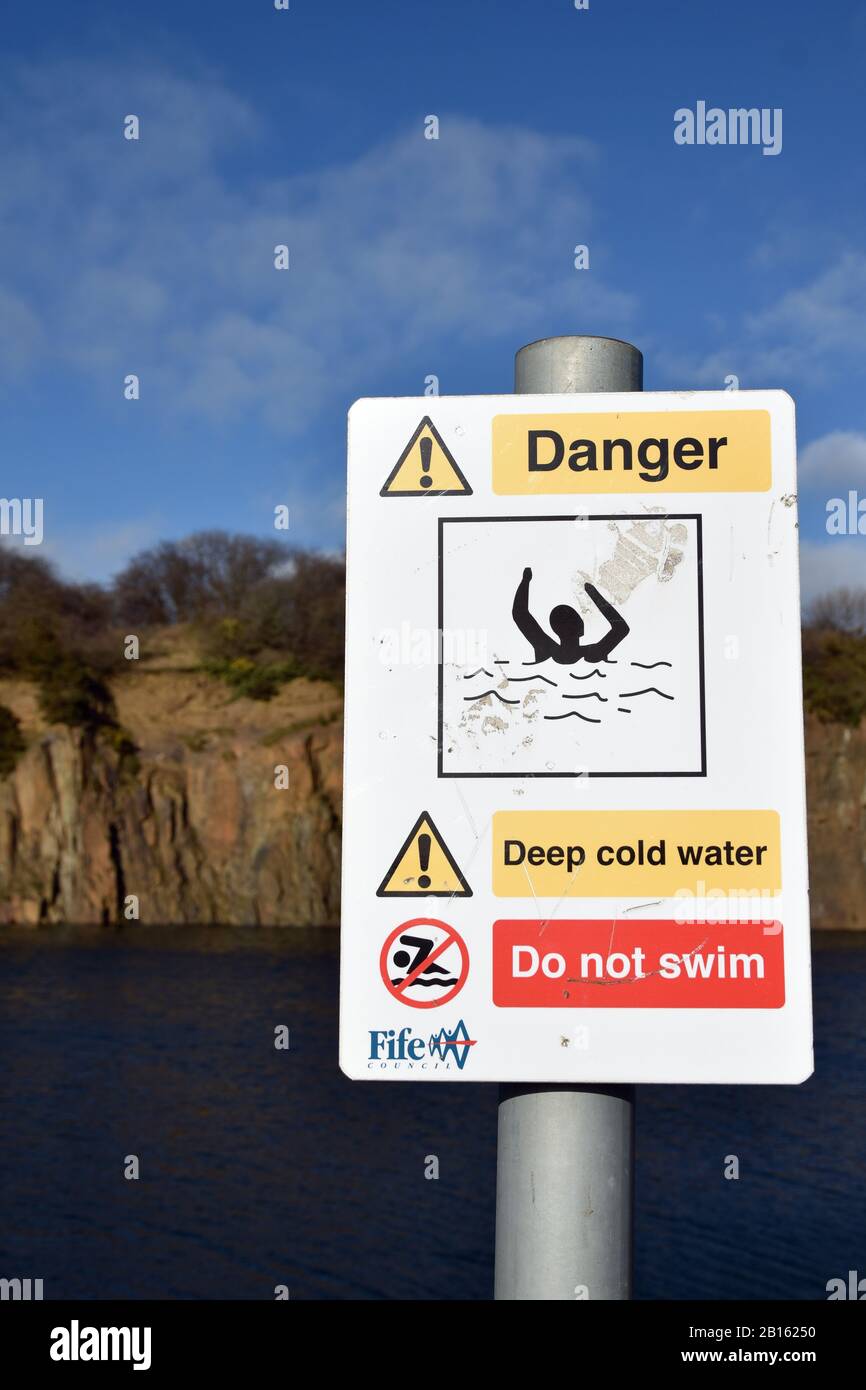Warning sign Prestonhill quarry Inverkeithing where deaths have occurred. Deep cold water, danger of drowning, do not swim. Blurred water, cliffs. Stock Photo