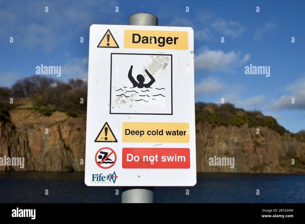 Warning sign Prestonhill quarry Inverkeithing where deaths have occurred. Deep cold water, danger of drowning, do not swim. Blurred water, cliffs. Stock Photo