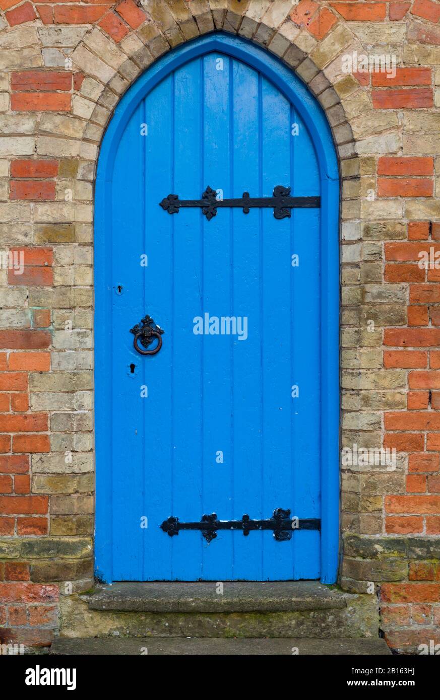 Traditional blue arched door with black ironmongery in a doorway, UK Stock Photo