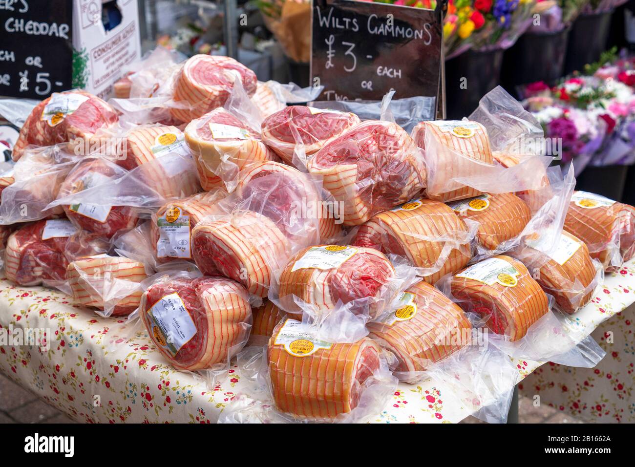 Shrink wrapped gammon bacon joints piled up on outdoor market stall table Stock Photo