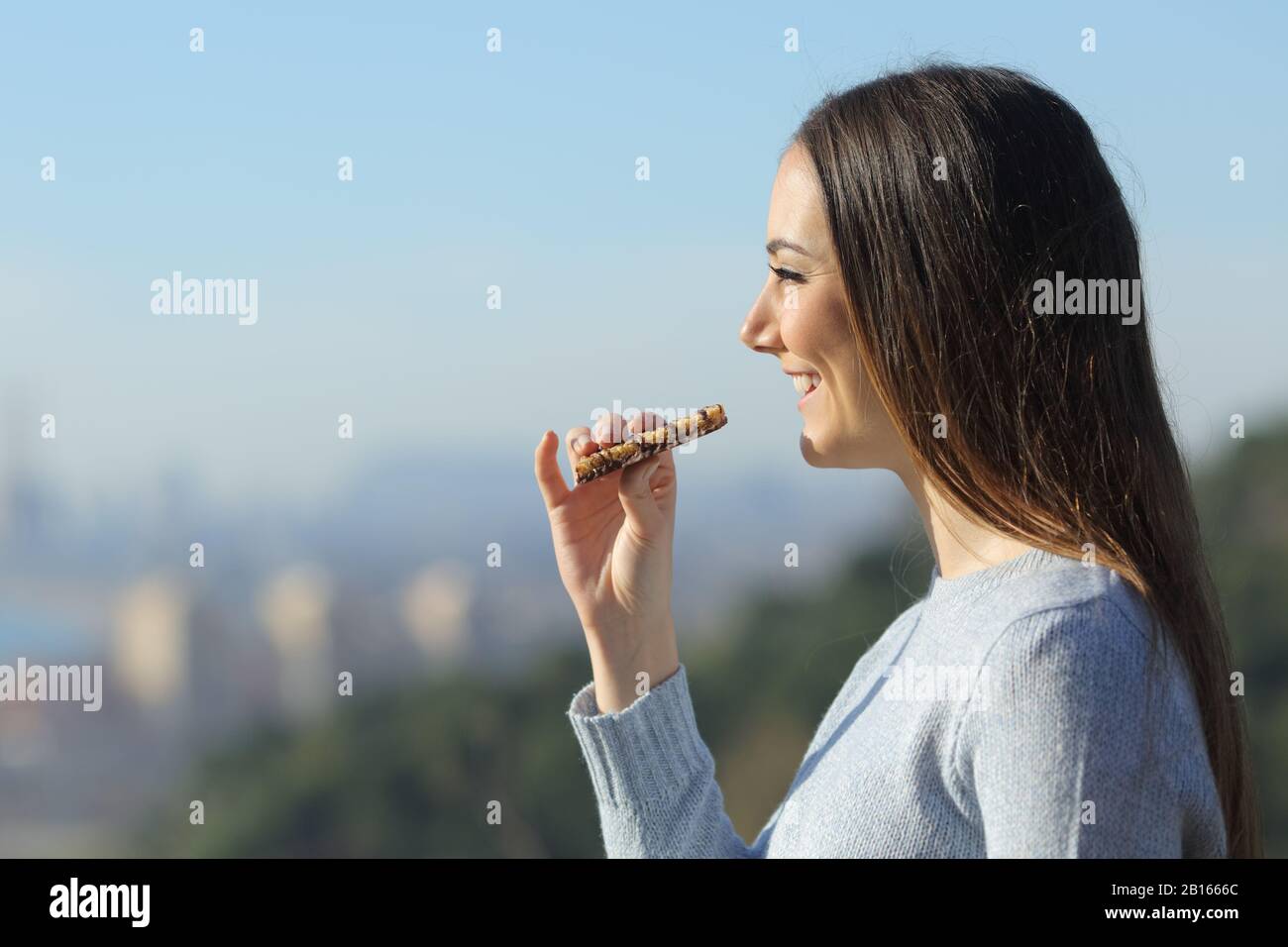 Happy girl eating a snack bar in the city outskirts while contemplating the views Stock Photo