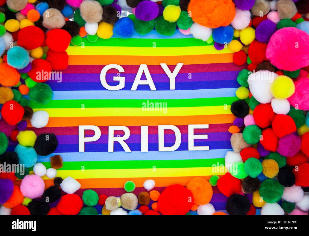 Gay Pride written on rainbow backdrop surrounded by rainbow coloured pompoms Stock Photo