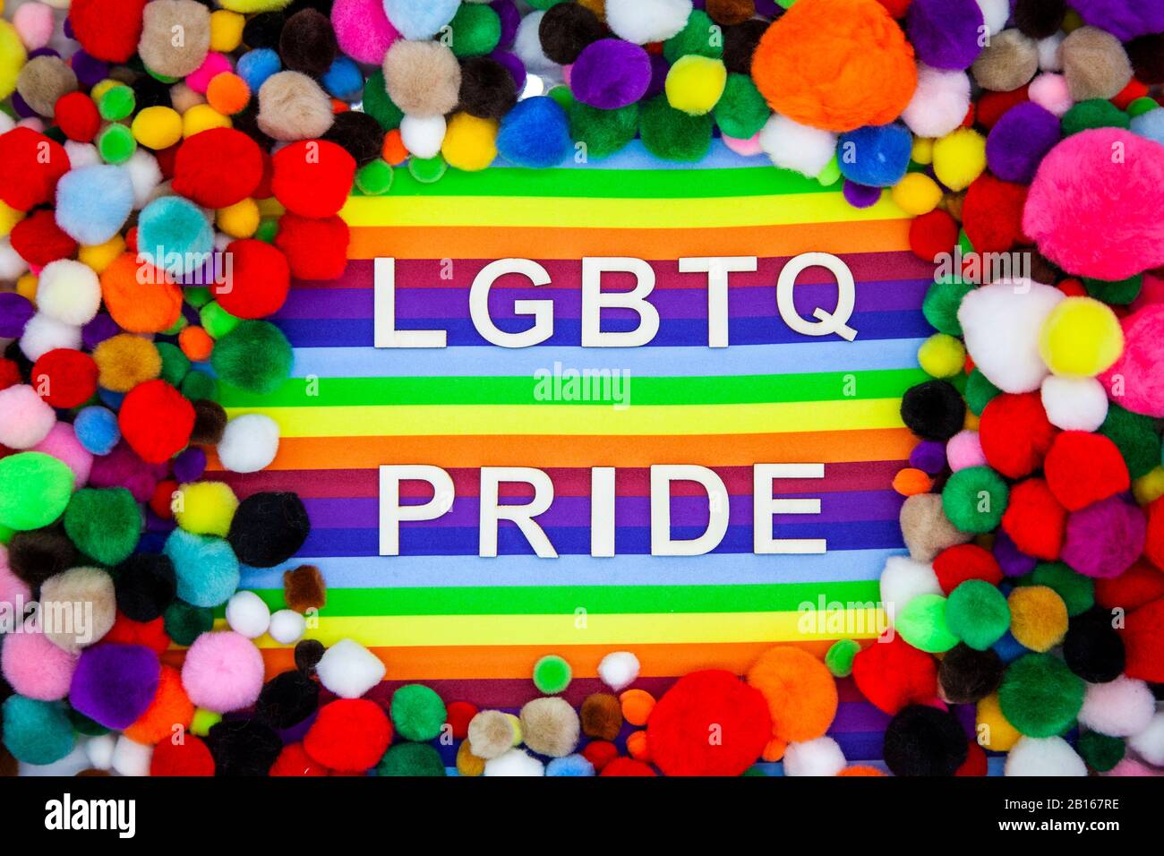 LGBTQ & Pride letters on rainbow backdrop surrounded by rainbow coloured pompoms Stock Photo