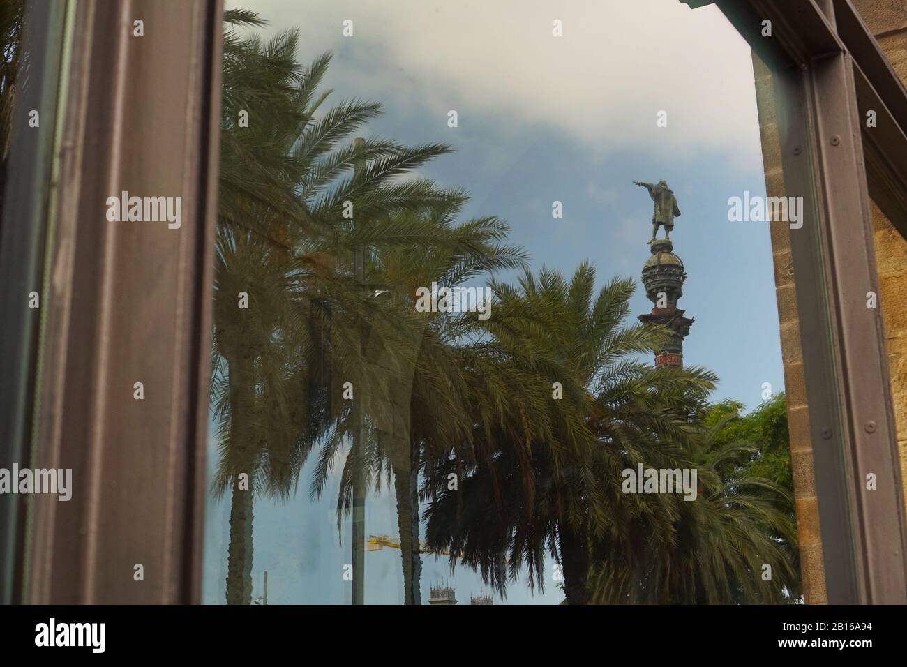 The reflection of Columbus statue pointing at the palm trees surrounded by the window frame Stock Photo