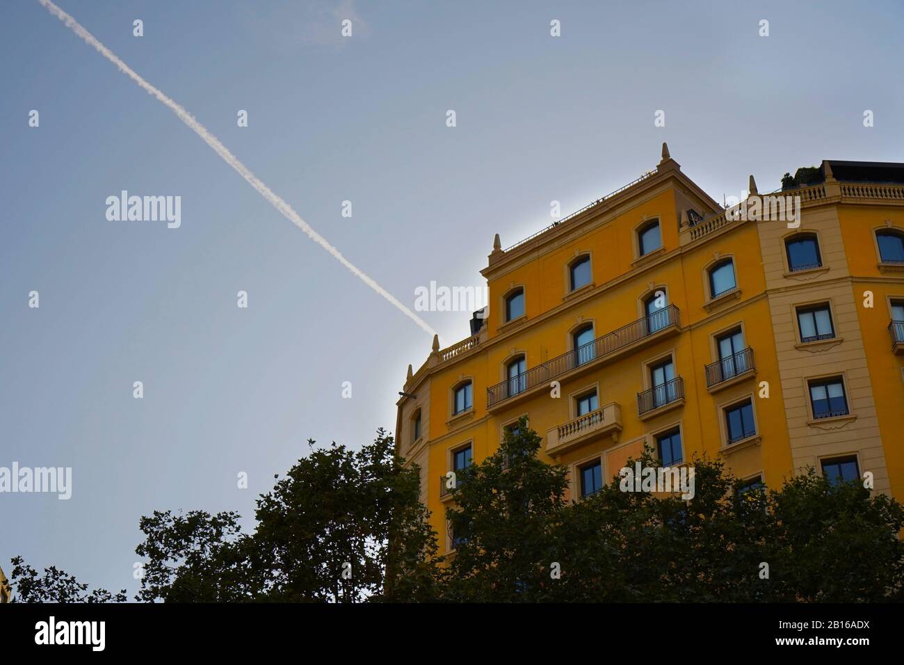 A bright yellow decorative apartment building surrounded by blue sky and a diagonal plane trail Stock Photo