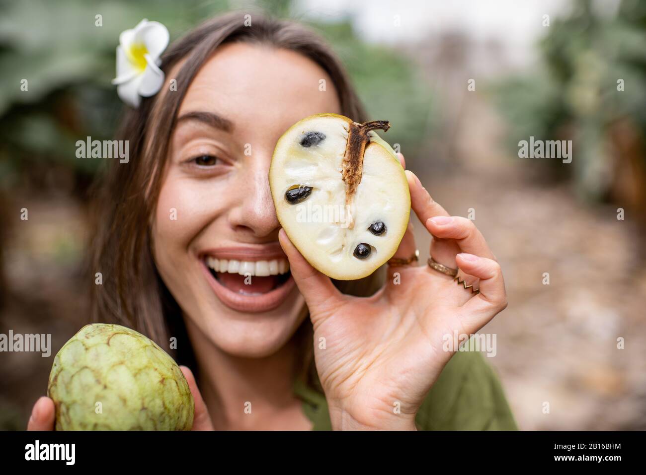 Closeup portrait of a young woman hiding her face behind Annona Cherimoya exotic fruit outdoors. Concept of vegetarianism, healthy eating fresh exotic fruits and wellbeing Stock Photo