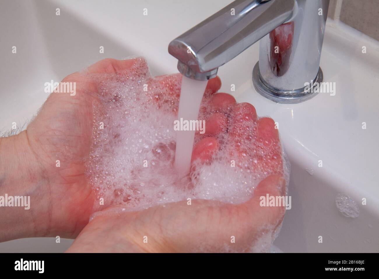Hands being washed in soapy water in a sink under a tap of running water. Cleanliness, hygiene and safely removing dirt, viruses and bacteria. Stock Photo