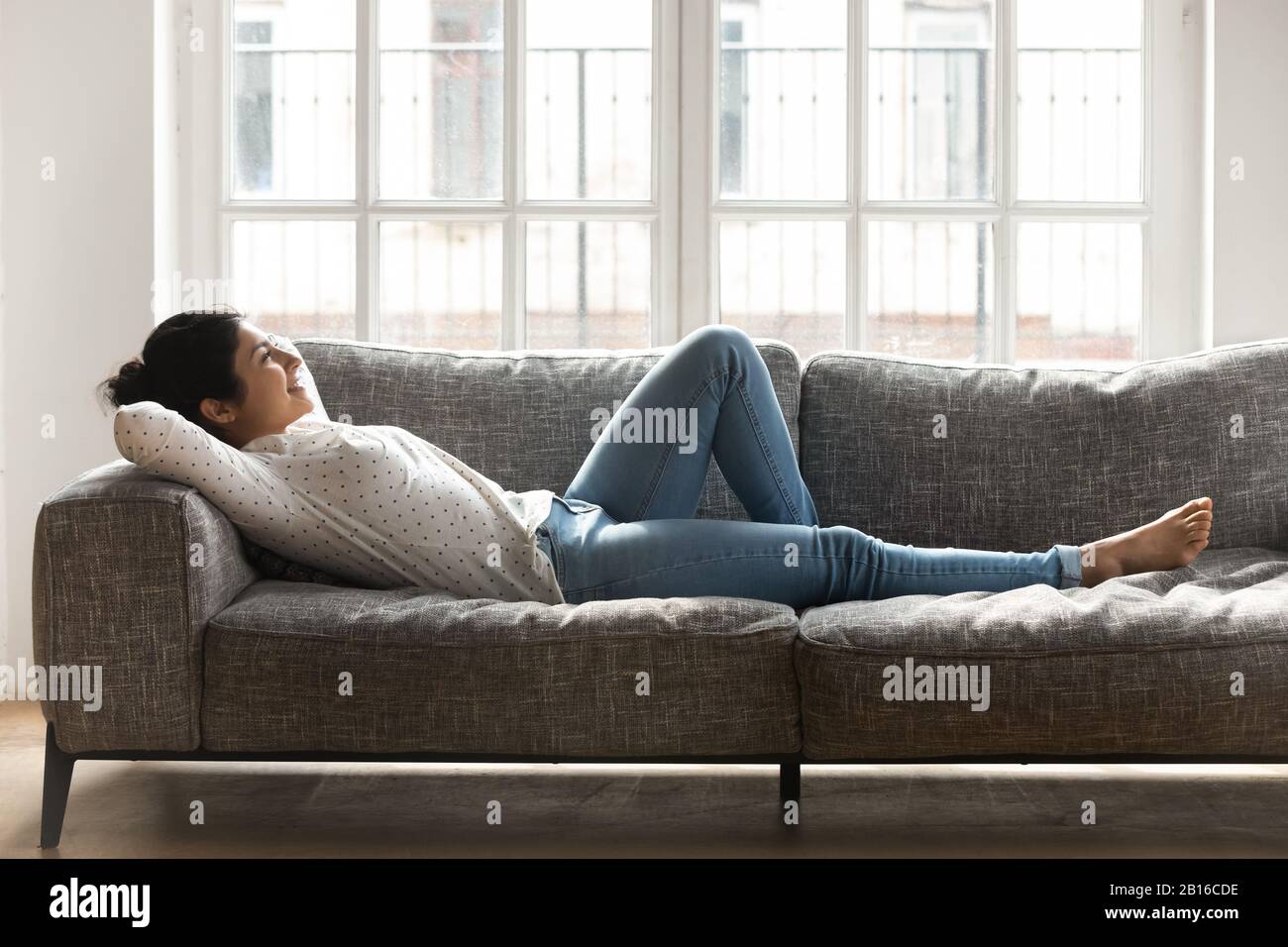 Woman lying on couch putting hands behind head enjoy vacation Stock Photo