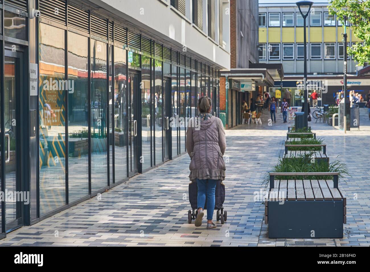 A lady pushing a pushchair past glass fronted office buildings in the centre of Stevenage, Hertfordshire Stock Photo