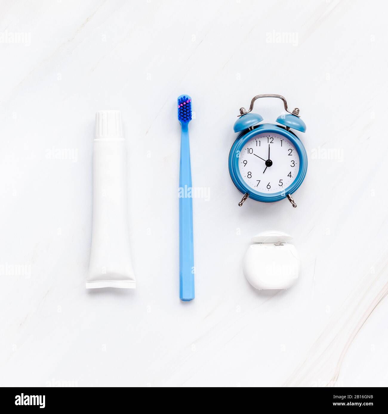 Teeth hygiene and oral dental care products with blue alarm clock on white marble table background with copy space. Blank tube of toothpaste and brush Stock Photo