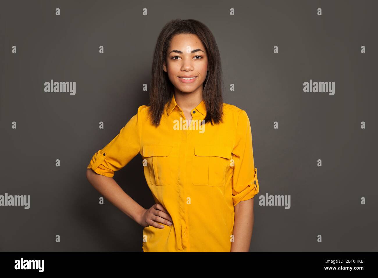 Portrait of happy successful black young woman in yellow shirt on gray ...